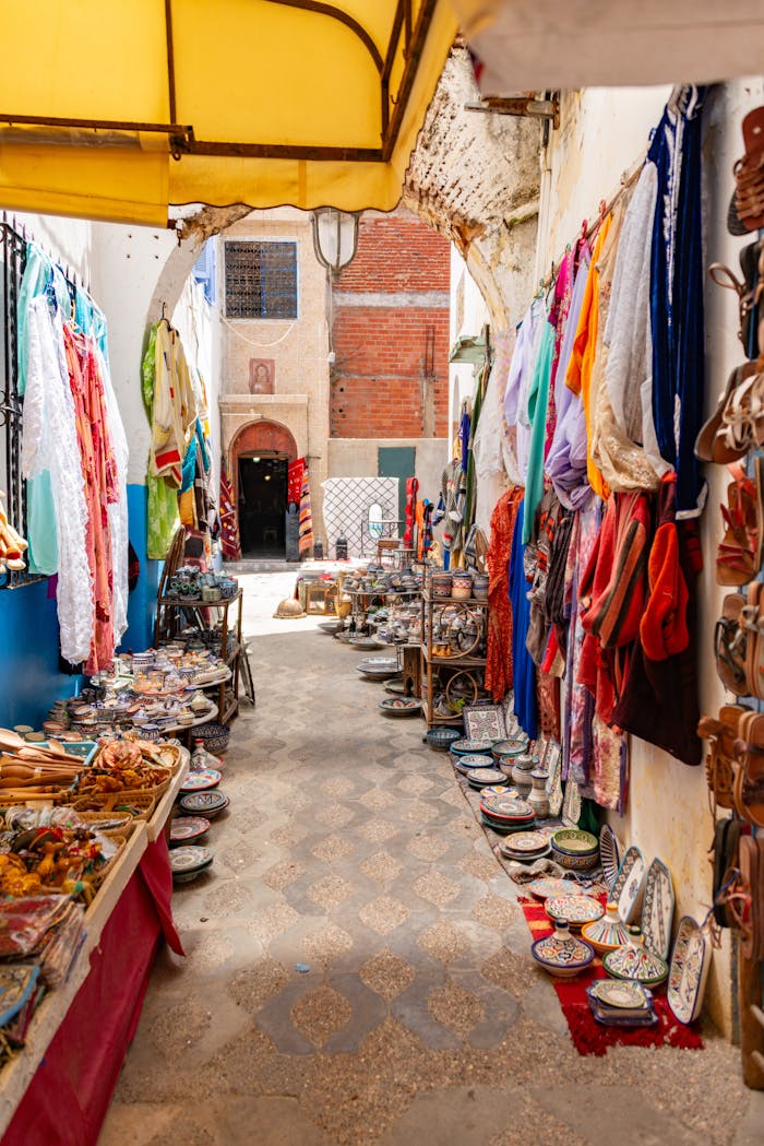 Explore a bustling alley in a Moroccan bazaar filled with textiles and pottery, bathed in summer sunlight.